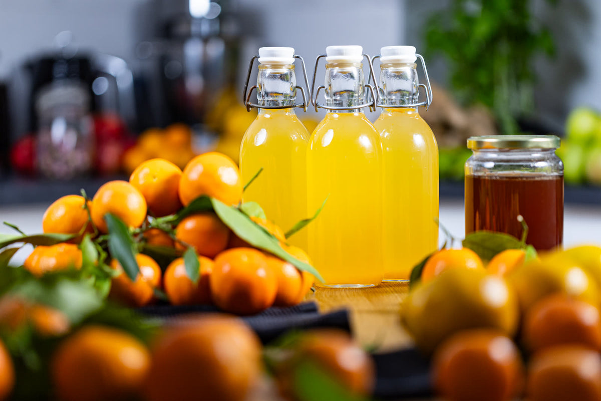 Boce narančaste kombuche od mandarine i meda, mandarine s lišćem i staklenka meda